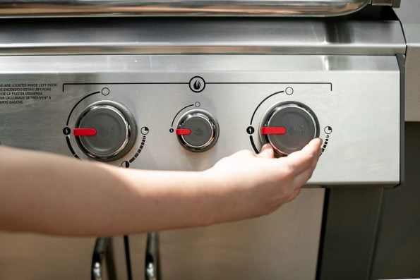 How to Start a Propane Grill, Step 4: A woman's shown opening the remaining burners of the Weber Genesis II to light the grill.