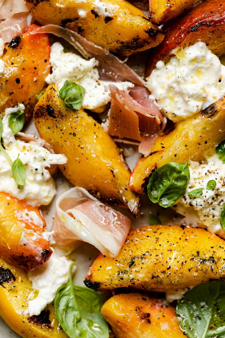 Close up of grilled peach burrata salad – grilled peaches, burrata cheese, thinly sliced prosciutto, & fresh basil leaves topped with flaky salt & freshly cracked pepper.