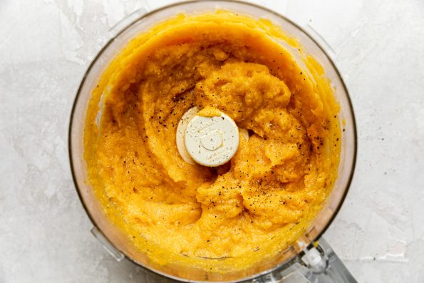 Roasted Garlic whipped Butternut Squash in a food processor bowl. The food processor bowl sits on top of a creamy cement surface.