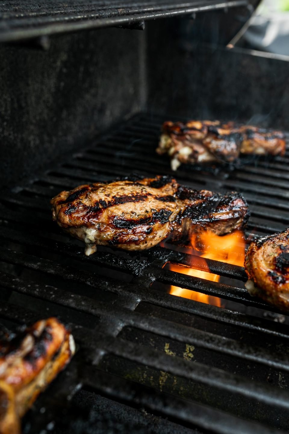 Stuffed bone in pork chops atop grilling grates with small flame flaring up through the grates.