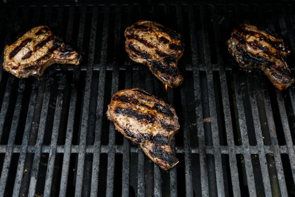 4 bone-in pork chops grilling on grill grates.