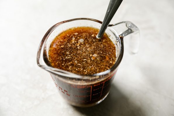 Ginger soy glaze ingredients mixed in a liquid measuring cup. There is a spoon in the cup & the cup sits atop a creamy cement surface.
