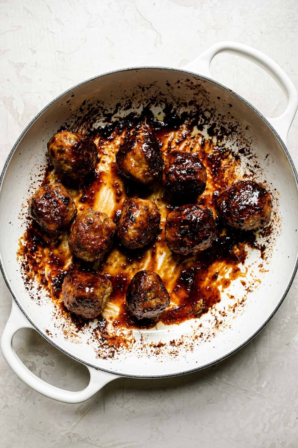 How to make ginger meatballs – glazed meatballs in white enameled braising pan atop a creamy cement surface.