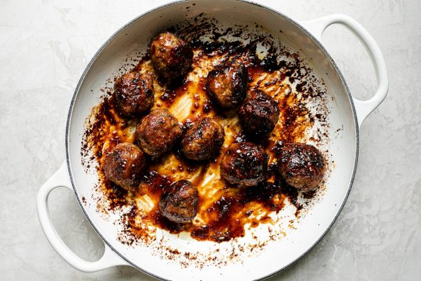 How to make ginger meatballs – glazed meatballs in white enameled braising pan atop a creamy cement surface.