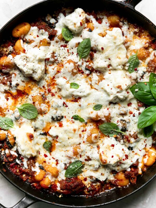 Overhead shot of baked gnocchi in a large oven-safe skillet, atop a creamy white surface. The pasta bake is garnished with fresh basil & ground black pepper.
