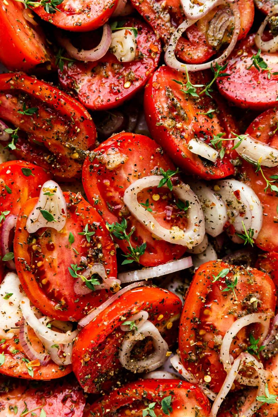 A close up shot of raw halved roma tomatoes with sliced shallots, & chopped garlic after being tossed in olive oil & Italian seasoning.