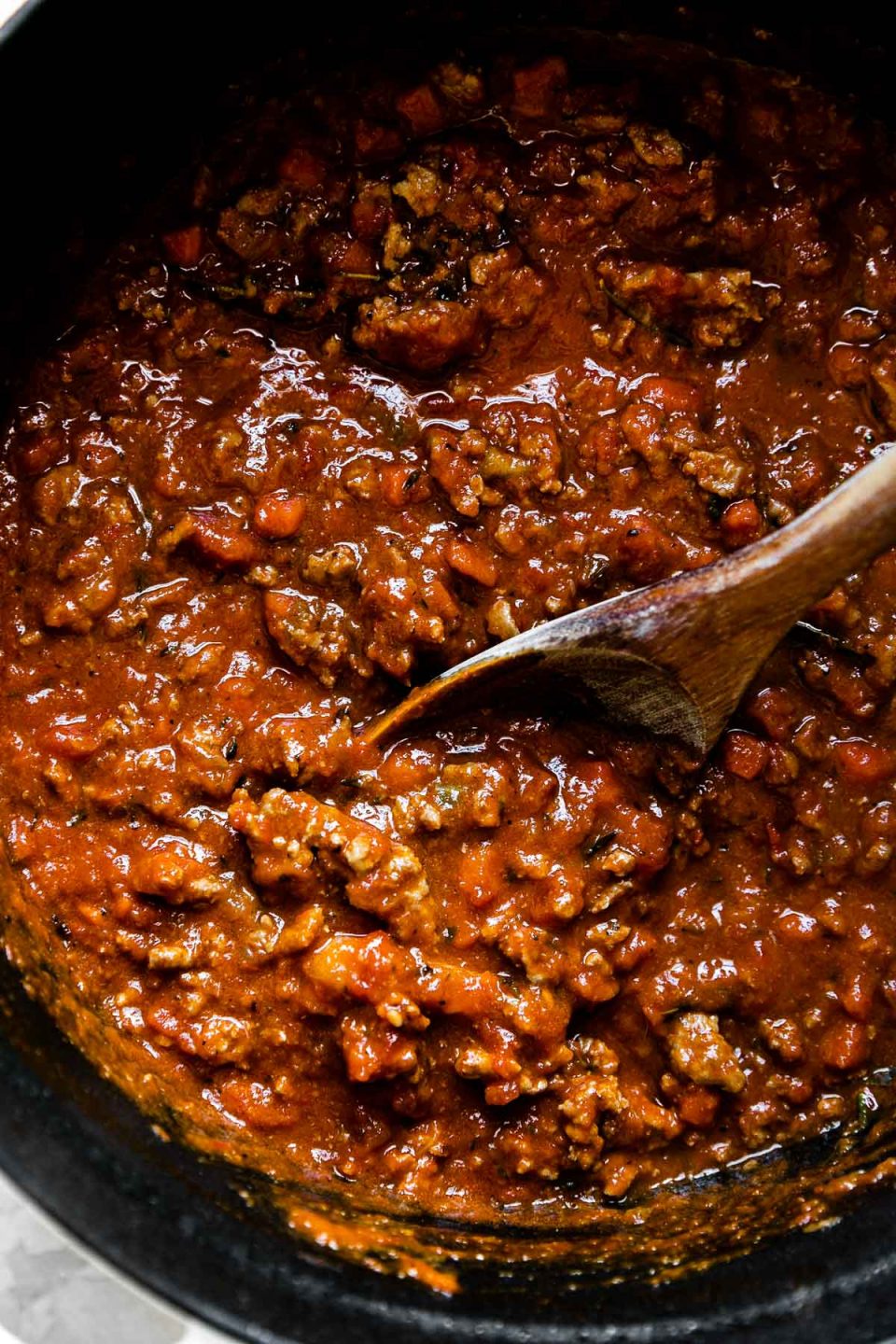 Weeknight bolognese sauce made with turkey in a large pot with a wooden spoon inside.