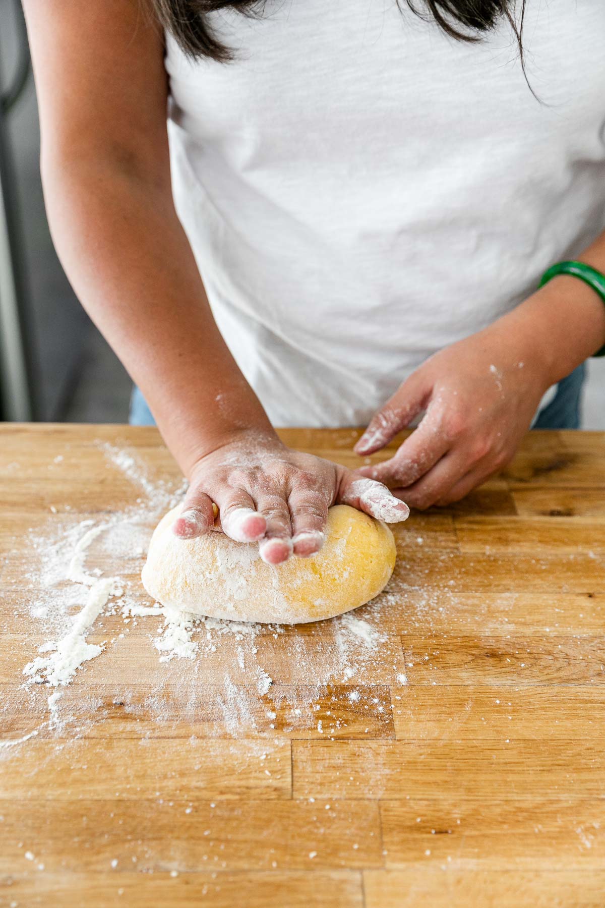How to Make Homemade Pasta, Step 3: Knead the Pasta Dough. Jess of Plays Well With Butter uses her hands to knead the fresh pasta dough ball until it becomes smooth & supple. The ​dough ball has been dusted with additional flour and is being kneaded on a clean butcher block countertop.