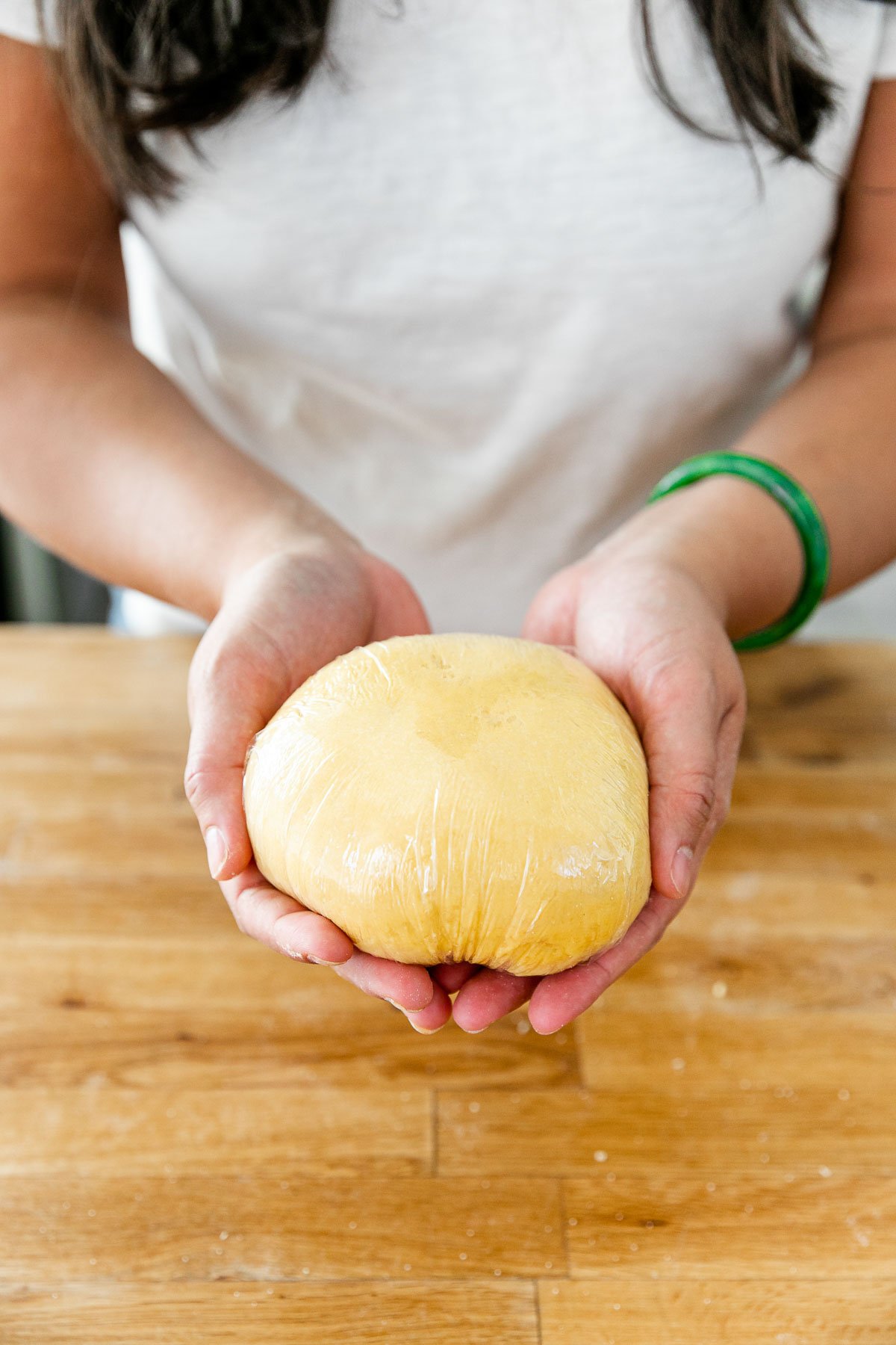 How to Make Homemade Pasta, Step 4: Rest the Pasta Dough. Jess of Plays Well With Butter holds a finished fresh pasta dough ball that has been tightly wrapped in plastic with both hands, ready to allow it to rest.