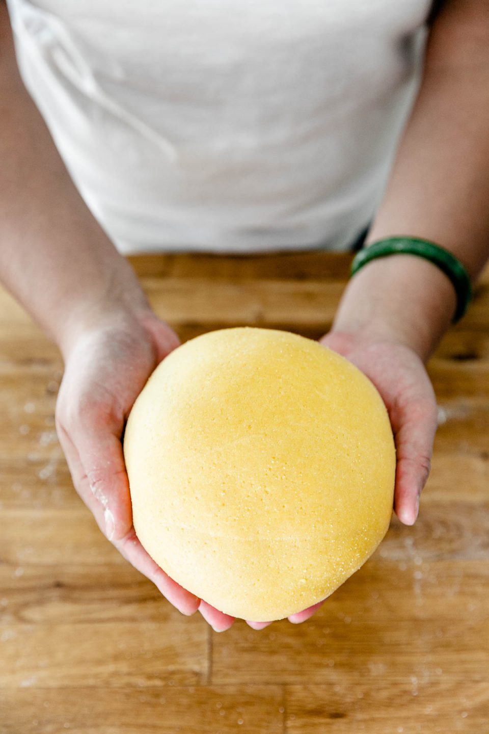 How to Make Fresh Pasta Dough with a Stand Mixer, Step 3: Rest the pasta dough. Jess of Plays Well With Butter holds a finished fresh pasta dough ball in both of her hands. The dough ball is smooth on the surface.