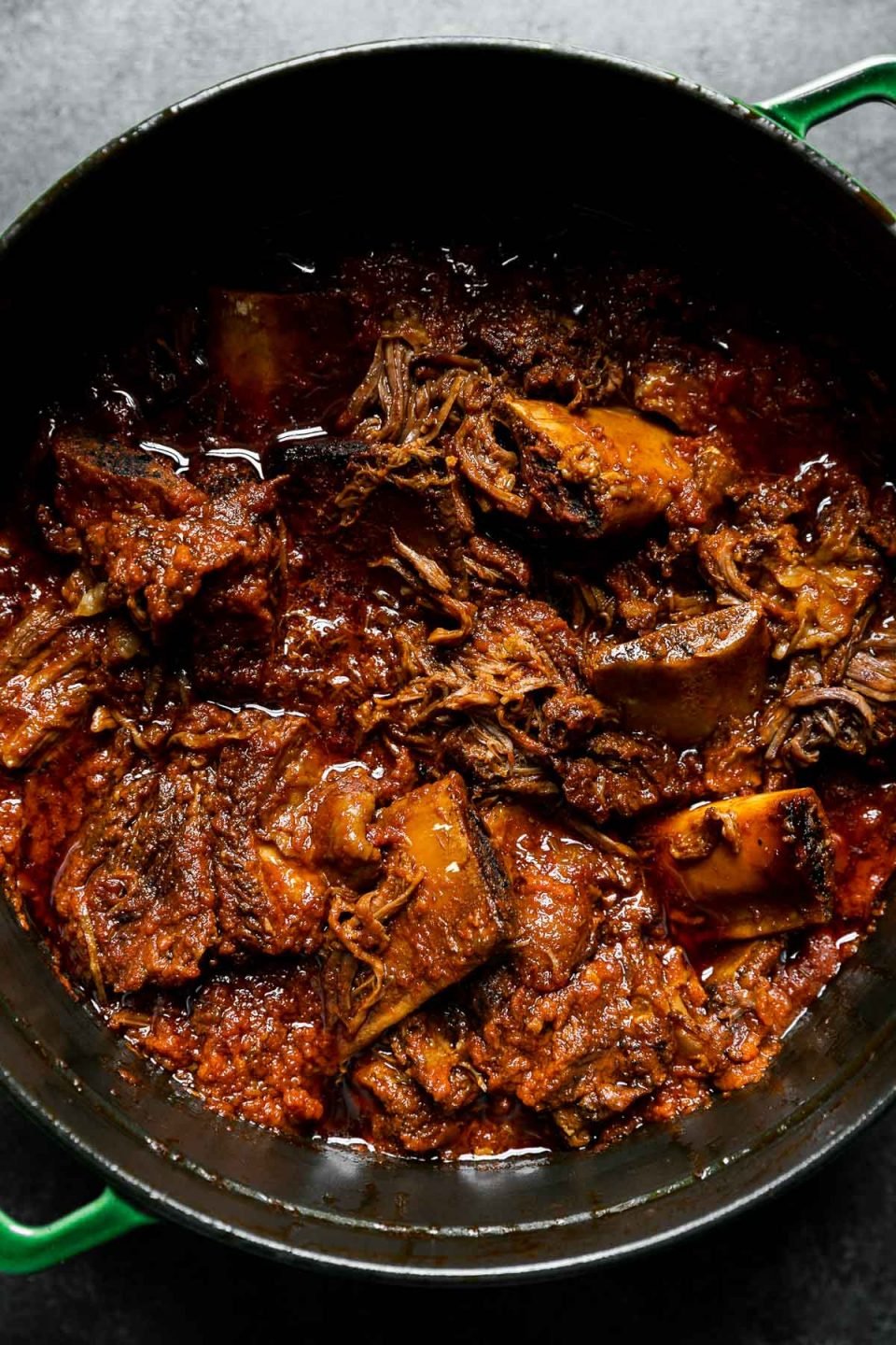 Slowly braised beef short rib ragu in a large Dutch oven atop a dark textured surface.