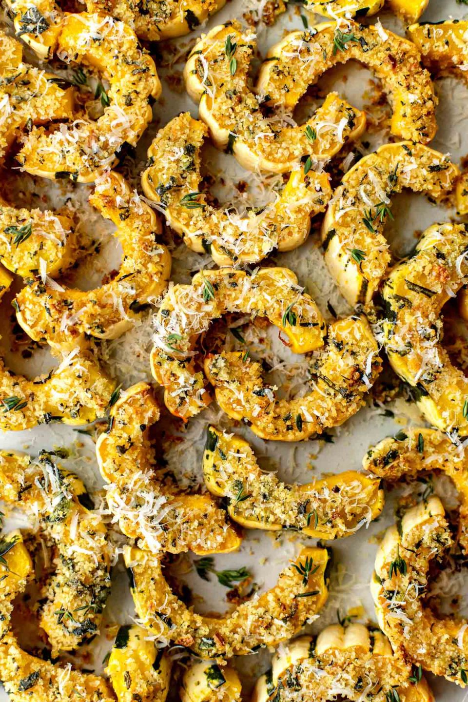 A close up shot of Parmesan Crusted Roasted Delicata Squash arranged on a creamy white serving platter. The squash has been garnished with freshly grated parmesan and fresh thyme.