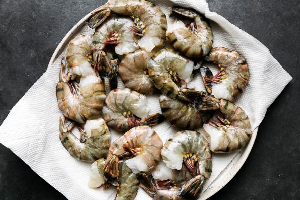 A paper towel-lined plate filled with thawed Black Tiger Shrimp rests atop a black textured surface.