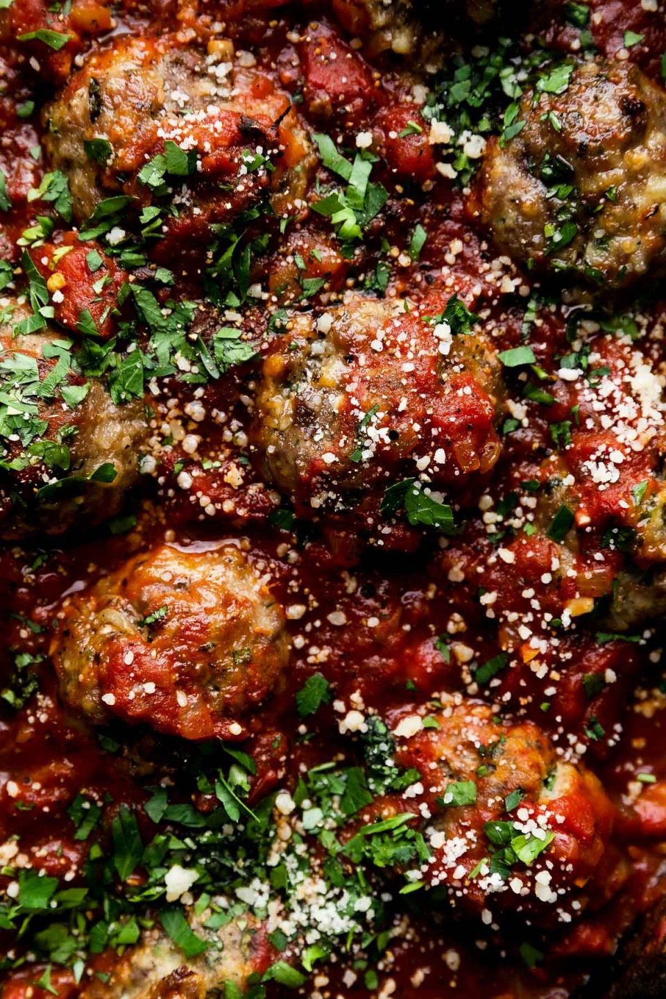 A close up shot of Best-Ever Italian Meatballs in a homemade simple red sauce. The meatballs have been garnished with freshly chopped basil, parsley, and parmesan cheese.