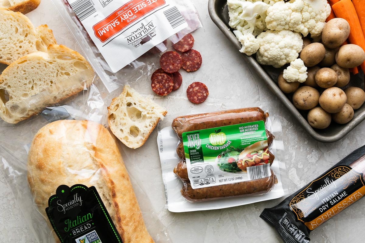 Cheese Fondue for Two ingredients arranged on a creamy white textured surface: baby potatoes, broccoli or cauliflower florets, carrots, Never Any! Apple Chicken Sausage, Specially Selected Italian Bread, and Appleton Farms Bite Size Salami.