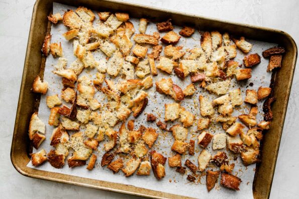 Homemade parmesan sourdough breadcrumbs arranged atop a baking sheet lined with parchment paper. The baking sheet sits atop a creamy white textured surface.