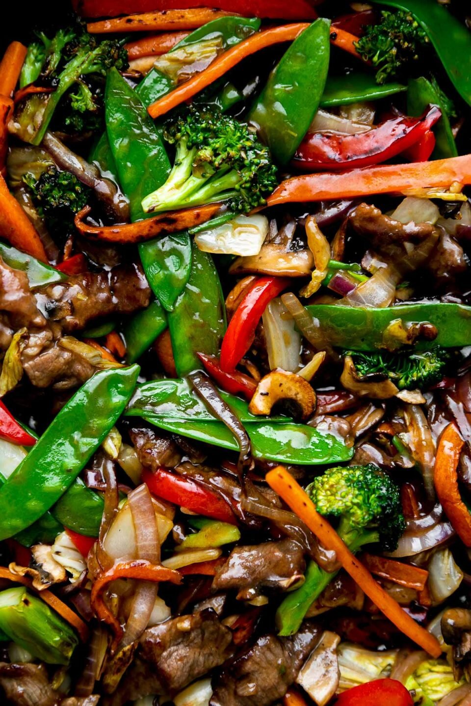 A close up macro shot of finished beef and vegetable stir fry. The beef and vegetables are glossy with a coating of homemade stir fry sauce.