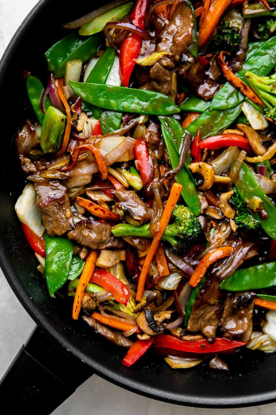 How to make beef and vegetable stir fry, step 4: Sear the beef & finish the stir fry. Finished beef vegetable stir fry fills a black Zwilling Madura Nonstick Skillet. The beef and vegetables are glossy with a coating of homemade stir fry sauce. The skillet sits atop a creamy white textured surface.