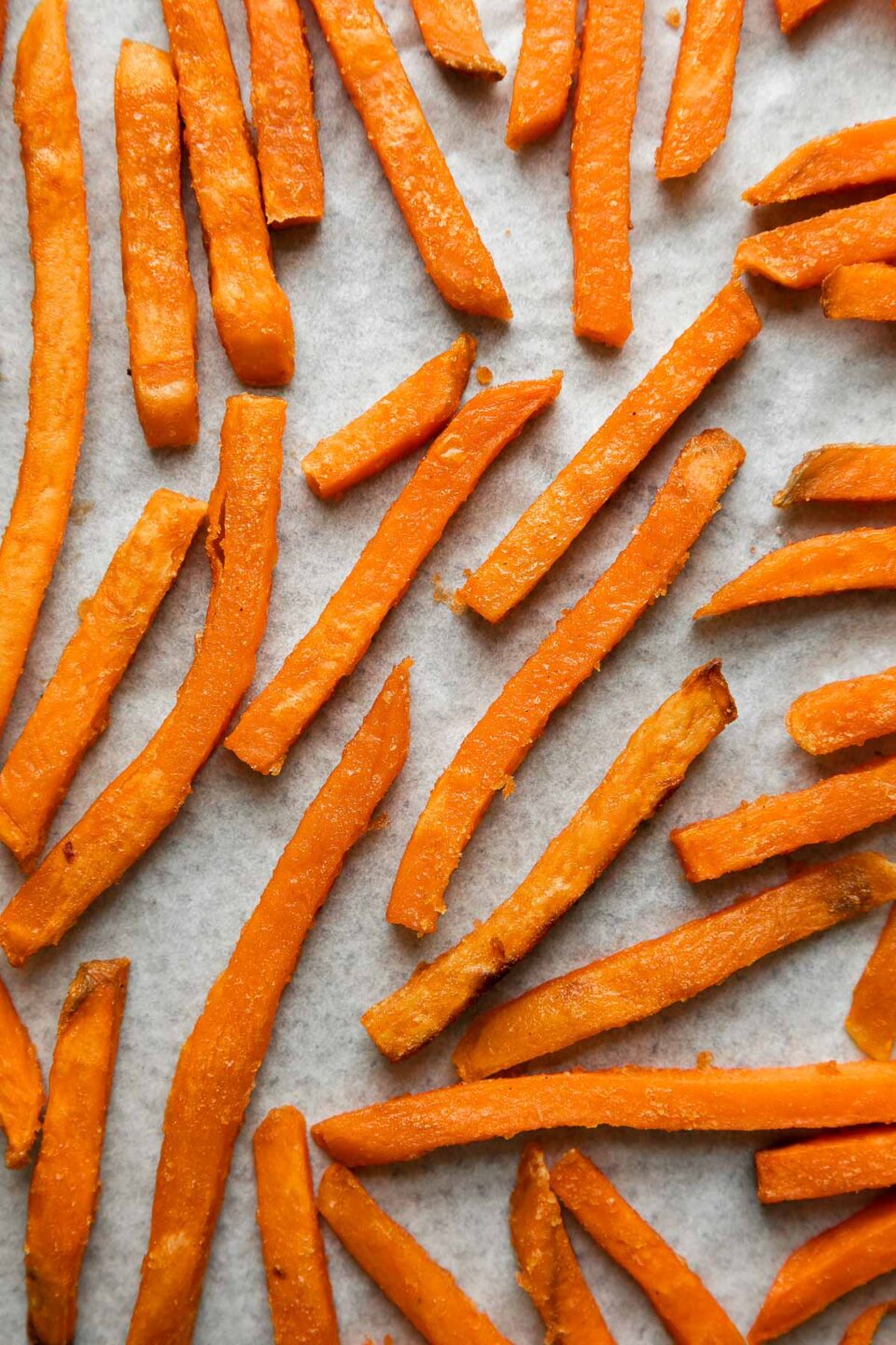 A close up of Alexia Sweet Potato Fries with Sea Salt arranged in a single layer on a parchment paper lined baking sheet.