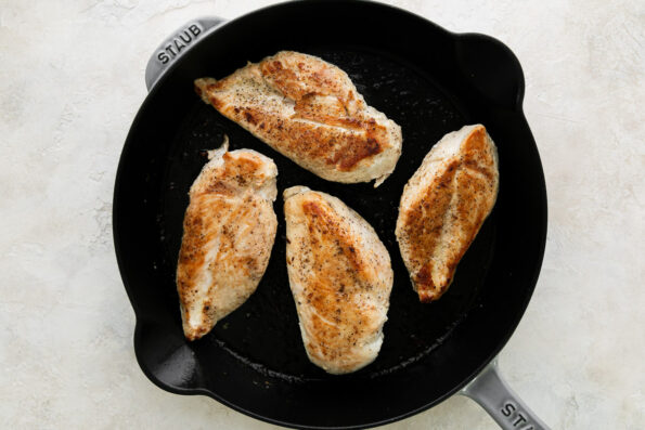 How to make French onion chicken, step 2: Sear the chicken. Four seasoned and seared chicken breasts rest inside of a grey Staub cast iron skillet. The skillet sits atop a creamy white textured surface.