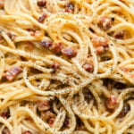 A close up shot of finished pasta carbonara garnished with ground black pepper.