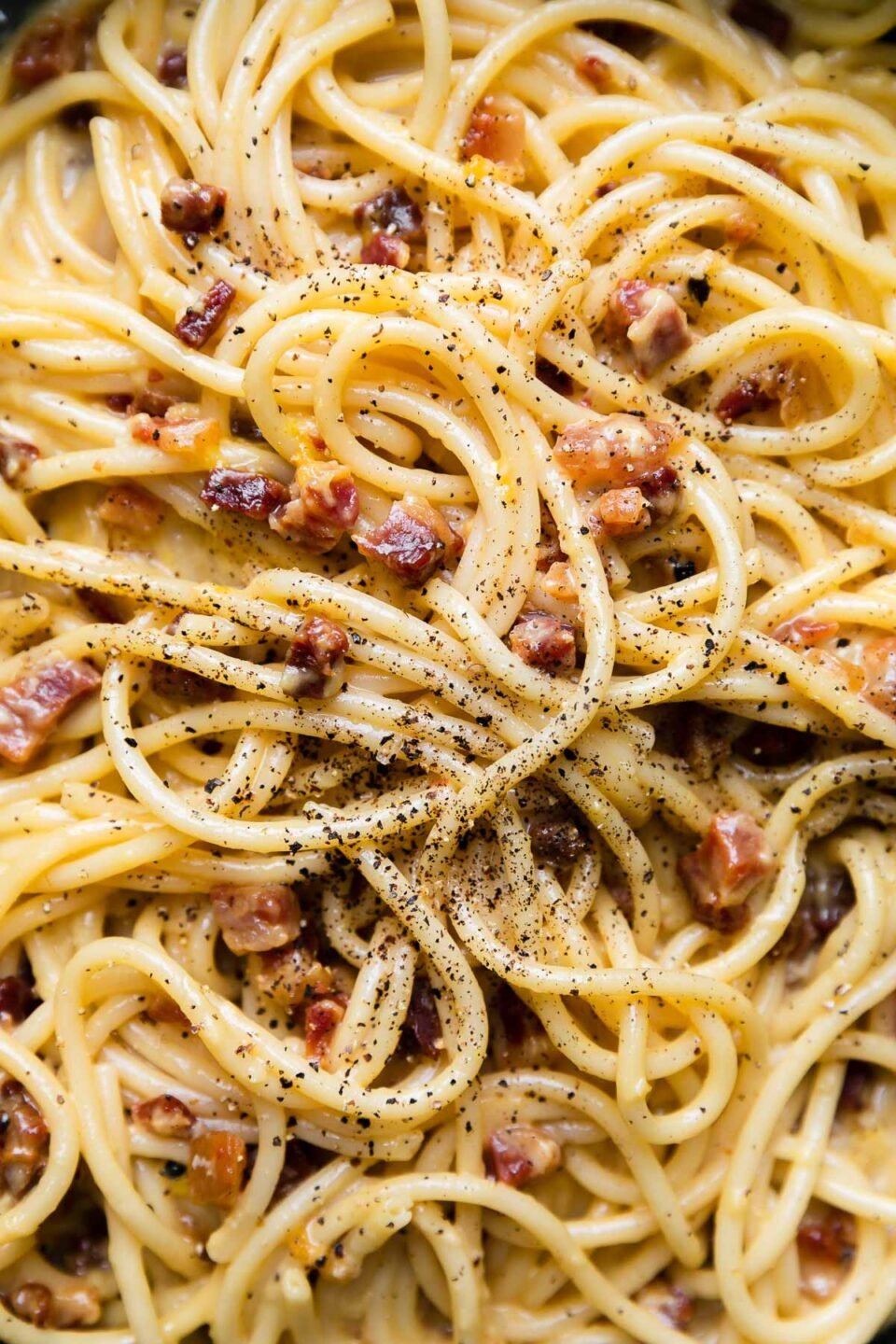 A close up shot of finished pasta carbonara garnished with ground black pepper.