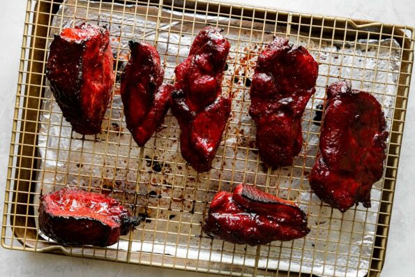 How to make Chinese BBQ pork, step 4: Roast the char siu pork. An aluminum foil lined baking sheet sits atop a creamy white textured surface. A wire rack sits atop the baking sheet with pieces of roasted char siu pork atop the rack.