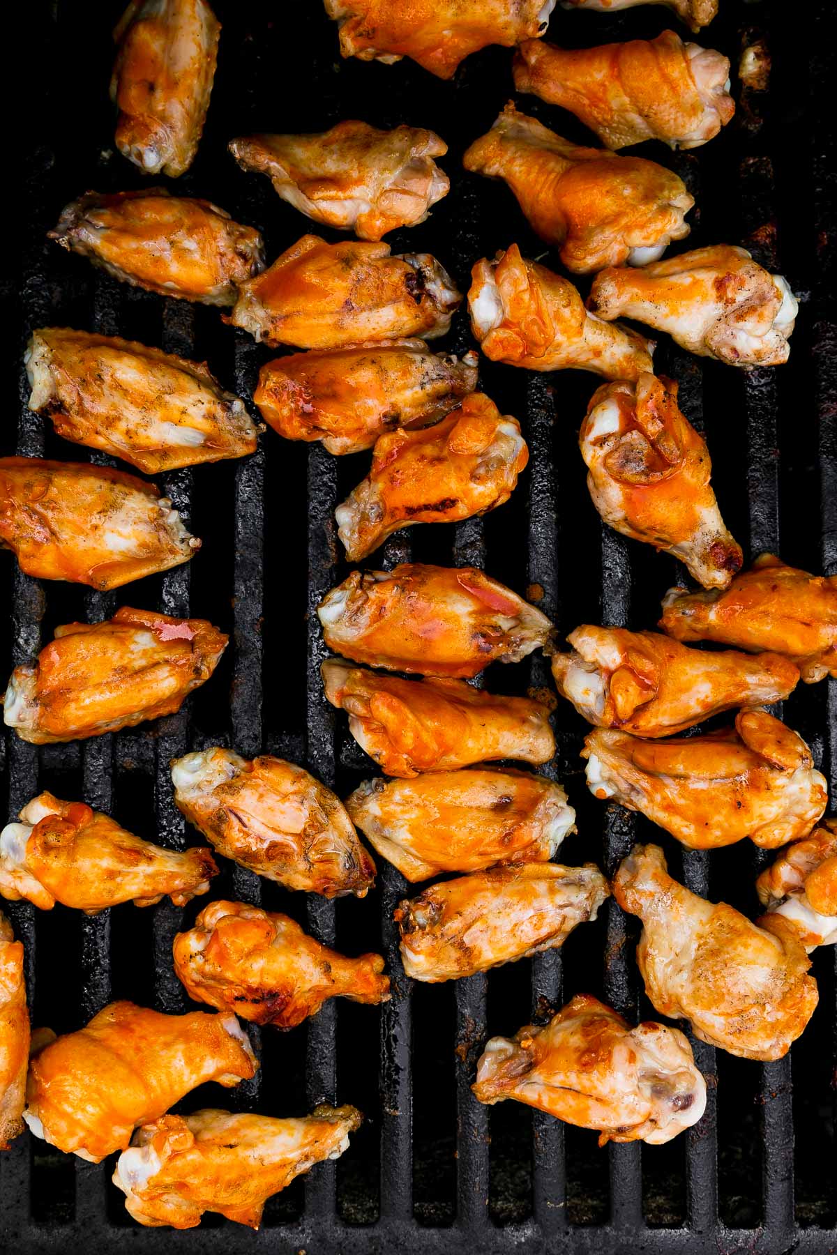 An overhead shot of brined chicken wings atop gas grill grates while they cook over indirect heat.