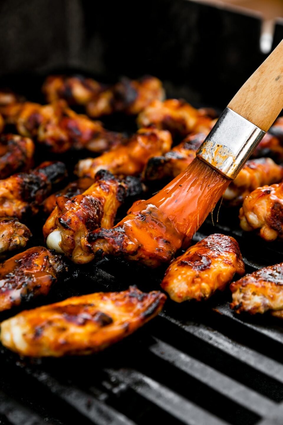 How to make grilled wings, step 4: Char the wings over direct heat. Grilled buffalo wings arranged on a gas grill over direct heat to char grill them. A pastry brush brushes additional Frank's RedHot over the wings.