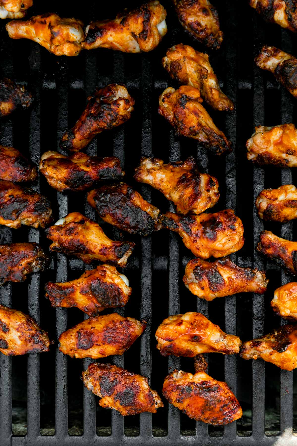 An overhead shot of grilled buffalo wings arranged on a gas grill over direct heat to achieve a char grill finish.