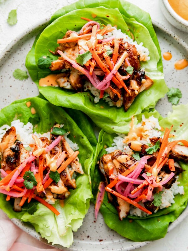 Three chicken bulgogi lettuce wraps filled with grilled chicken bulgogi, white rice, pickled vegetables, shredded carrots, cilantro, and a drizzle of creamy orange sauce, served on a speckled plate.
