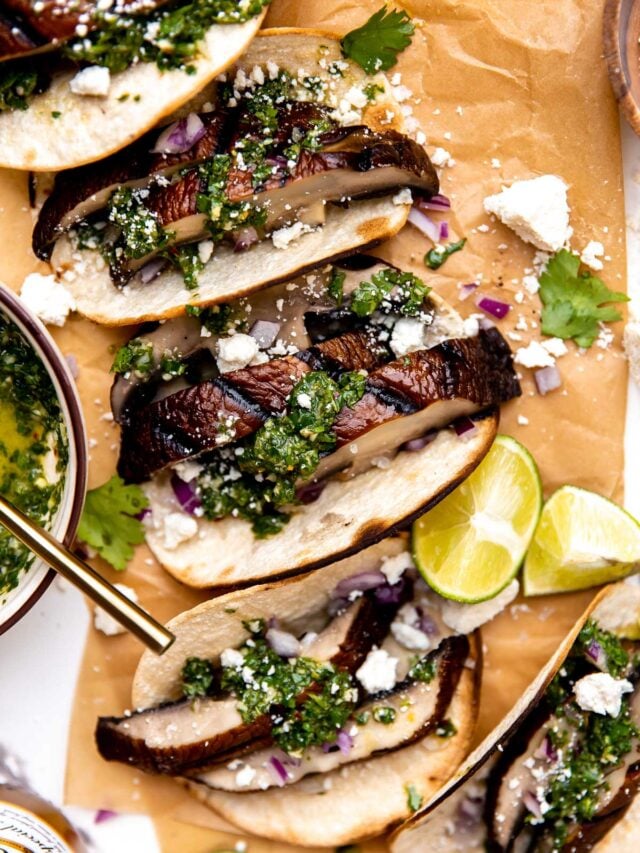 An overhead shot of mushroom tacos on a piece of brown parchment paper, garnished with chimichurri sauce, cojita cheese, red onions and cilantro. 
