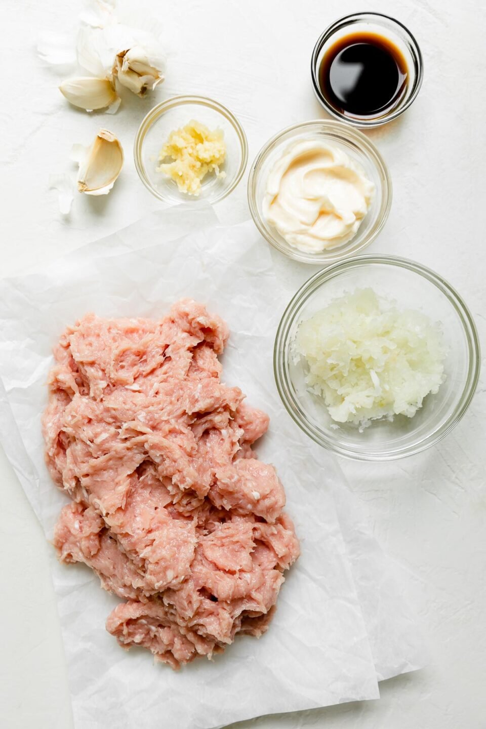 Ground chicken, yellow onion, garlic, mayonnaise, Worcestershire sauce arranged on a creamy white textured surface.