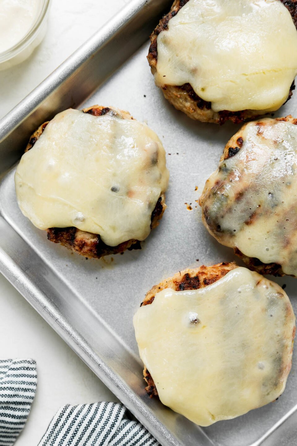 Four chicken burger patties with melted cheese sits atop a small aluminum baking sheet.