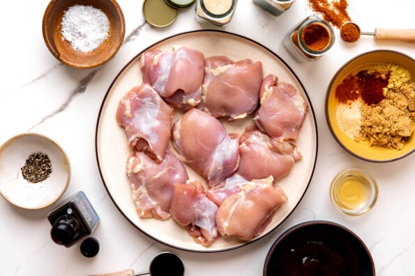 Shredded BBQ chicken ingredients arranged on a white and gray marble surface: boneless, skinless chicken thighs or breasts, Plays Well With Butter dry rub, olive oil, apple cider vinegar, Worcestershire sauce, liquid smoke.