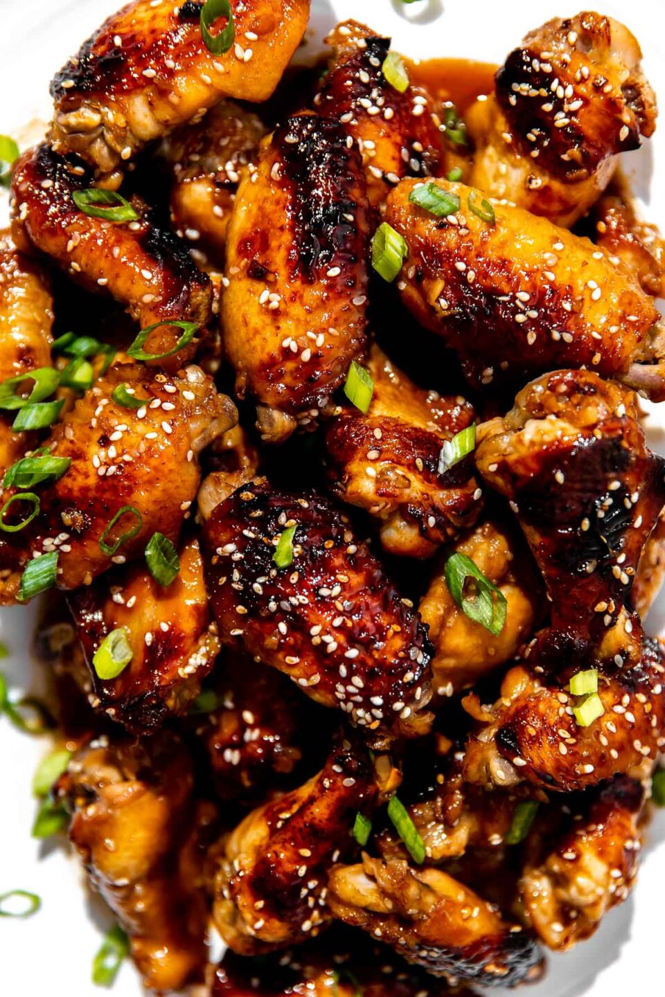 An overhead shot of finished sesame chicken wings atop a white ceramic serving platter. The sesame wings have been garnished with additional sesame seeds and thinly sliced green onion.