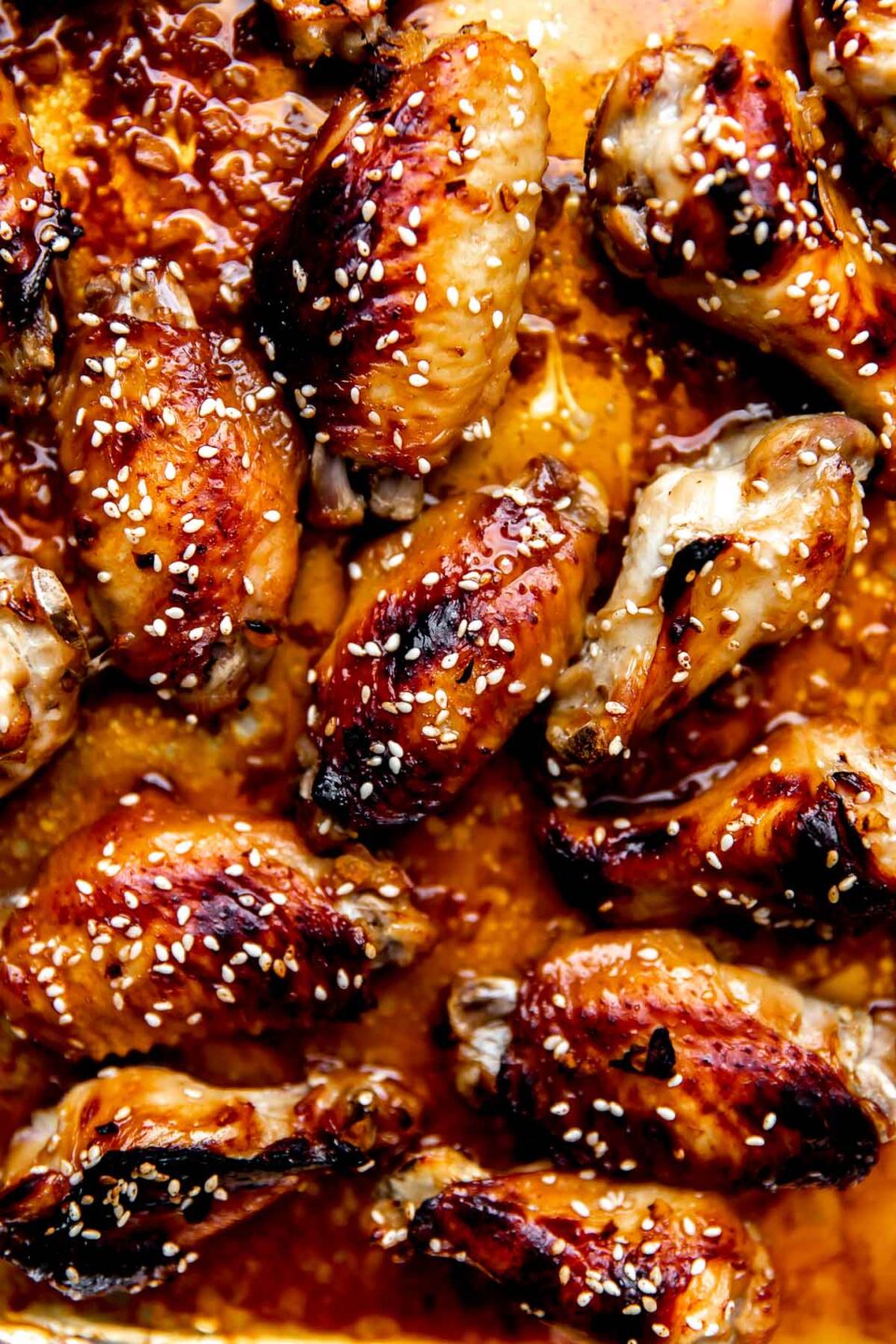A close up and macro shot of baked honey sesame chicken wings atop an aluminum lined baking sheet.