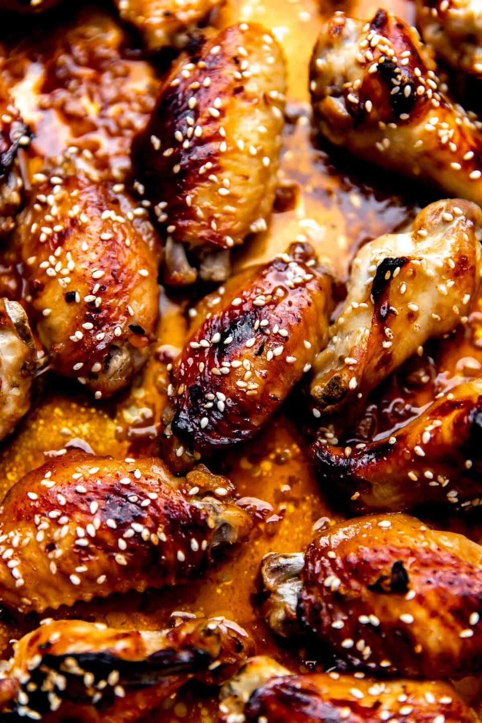 A close up and macro shot of baked honey sesame chicken wings atop an aluminum lined baking sheet.