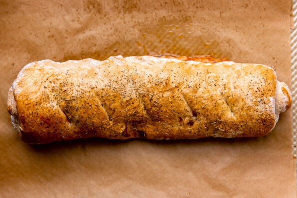 A finished Italian meat stromboli rests atop a parchment lined baking sheet.