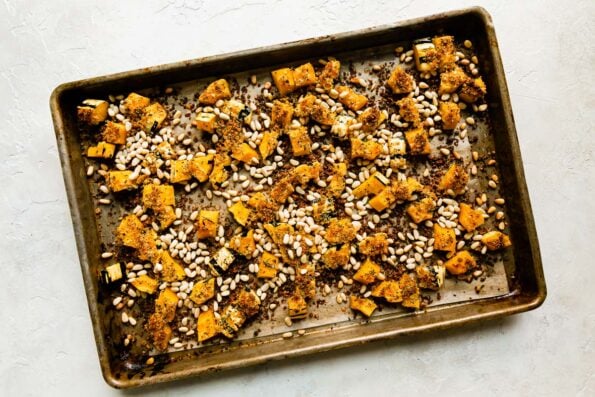 Roasted delicata squash "croutons" for autumn caesar salad are arranged atop a baking sheet pan that sits atop a creamy white textured surface.