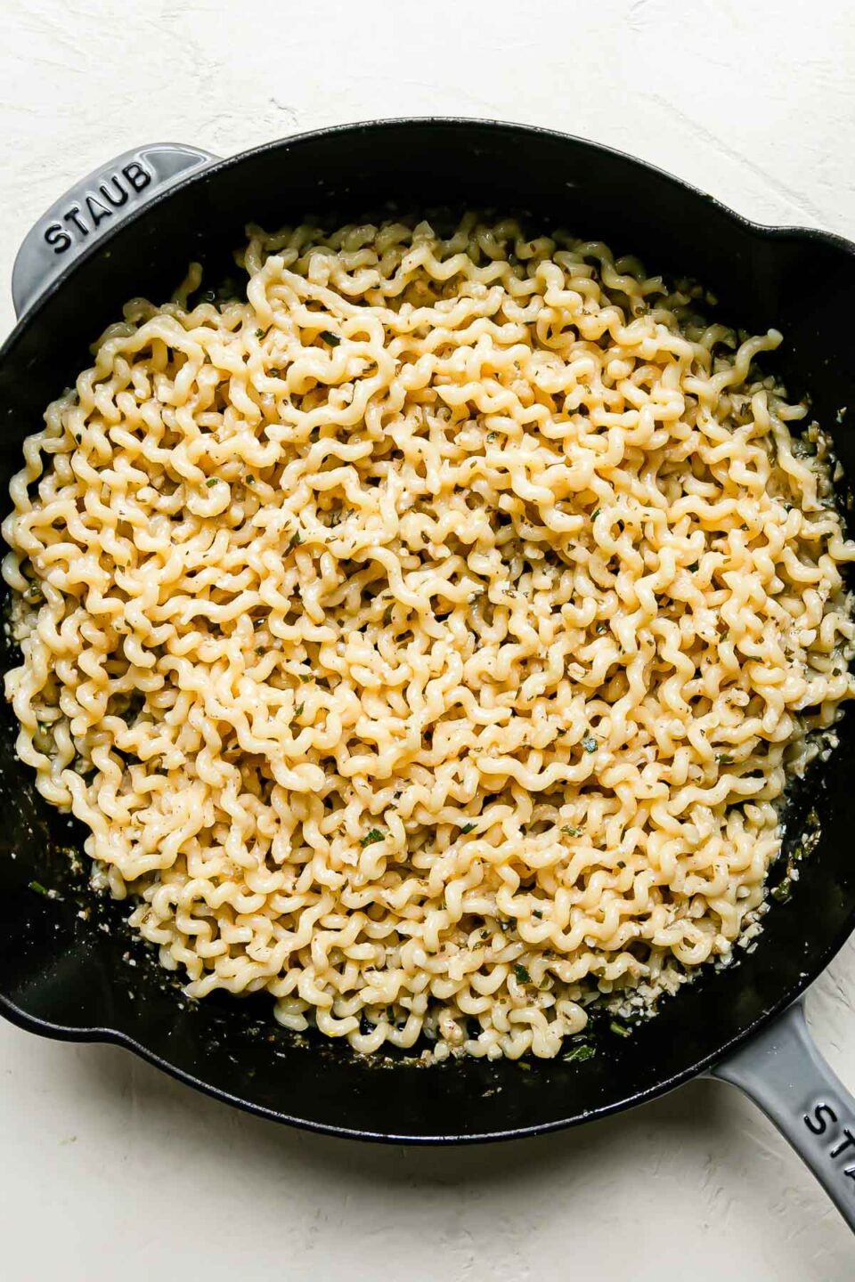 Brown butter pasta fits a light gray Staub cast iron skillet that sits atop a creamy white textured skillet.