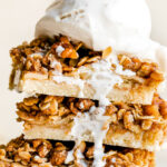 A side angle shot of three easy apple pie bars stacked on top of each other served with a scoop of vanilla ice cream melting over top.
