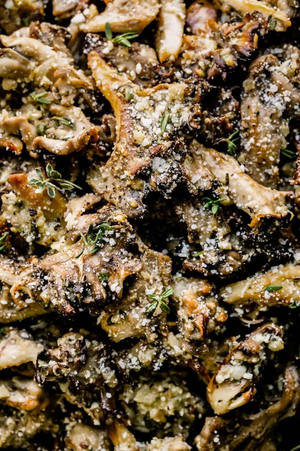A close up macro shot of roasted mushrooms garnished with grated parmesan cheese and finely chopped fresh herbs.