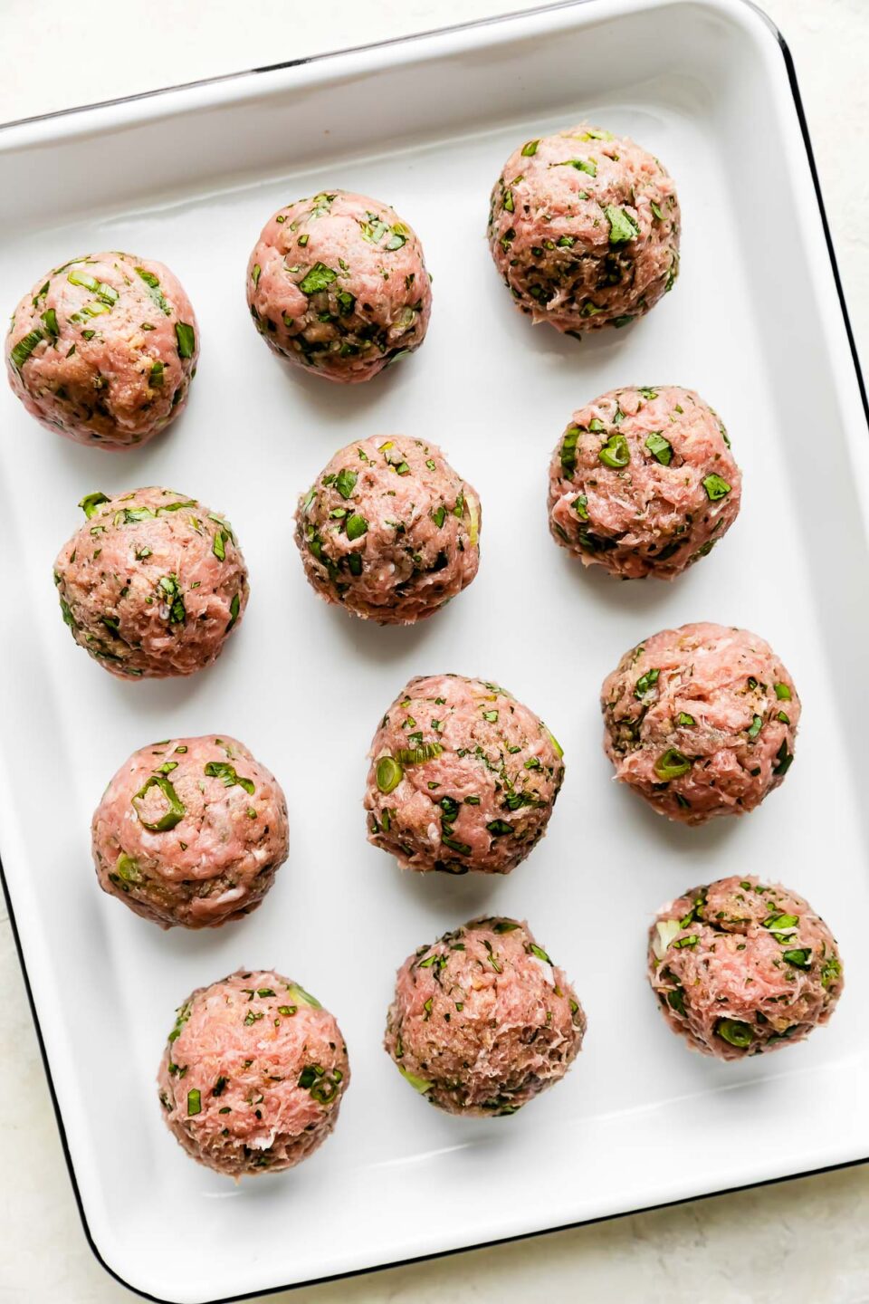 Twelve ground turkey or chicken curry meatballs are arranged atop a white ceramic baking dish. The baking dish sits atop a creamy white textured surface.