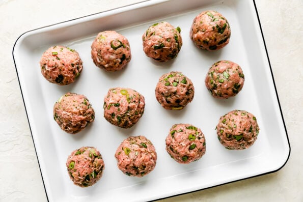 Twelve ground turkey or chicken curry meatballs are arranged atop a white ceramic baking dish. The baking dish sits atop a creamy white textured surface.