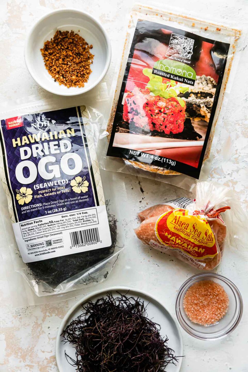 Ahi poke ingredients arranged on a creamy white textured surface: Inamona, Hawaiian dried ogo, and Hawaiian sea salt.