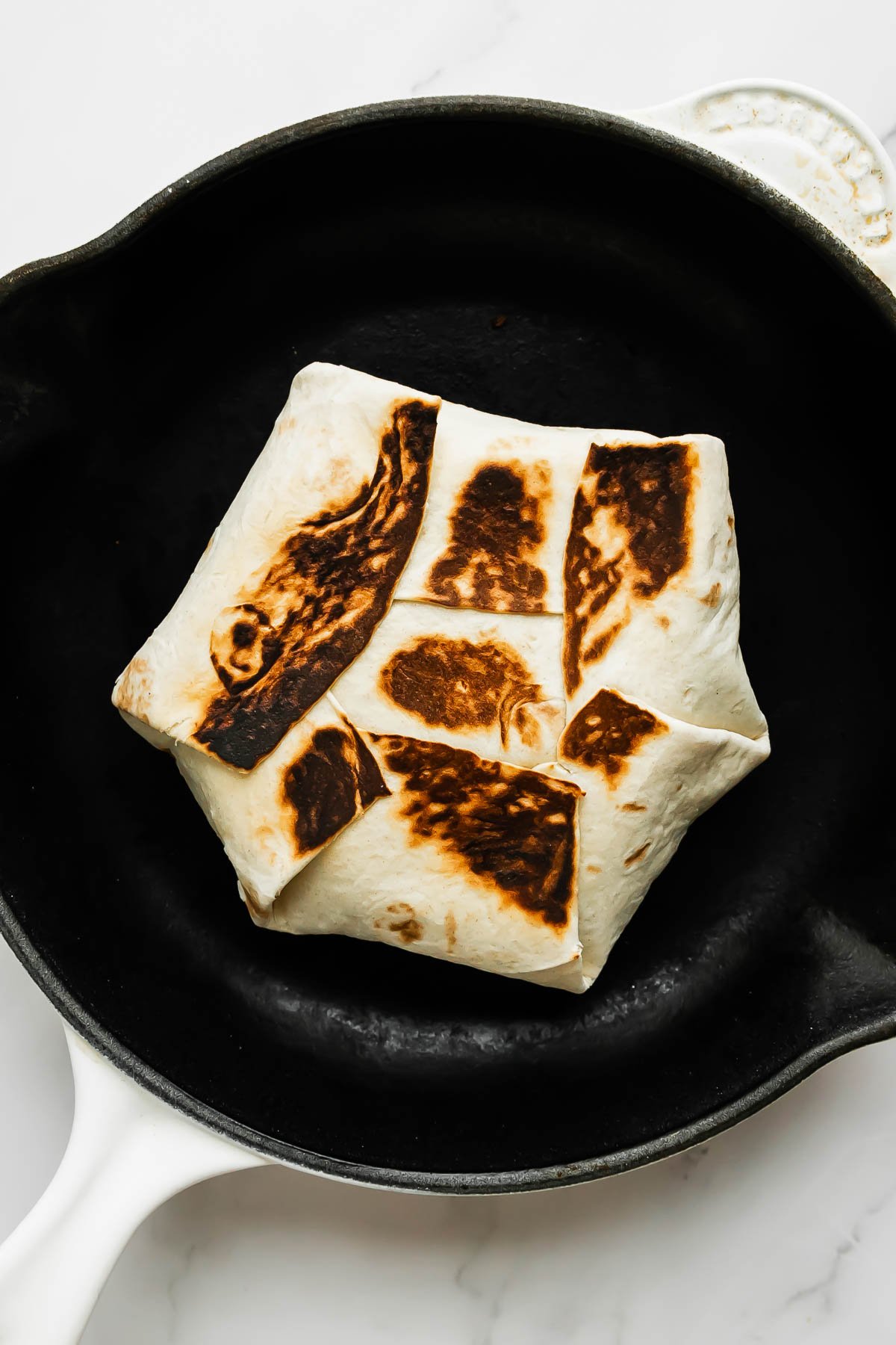 Three stacked buffalo chicken crunchwrap halves sit atop a white and gray marble surface. Sliced green onion rests in the foreground.