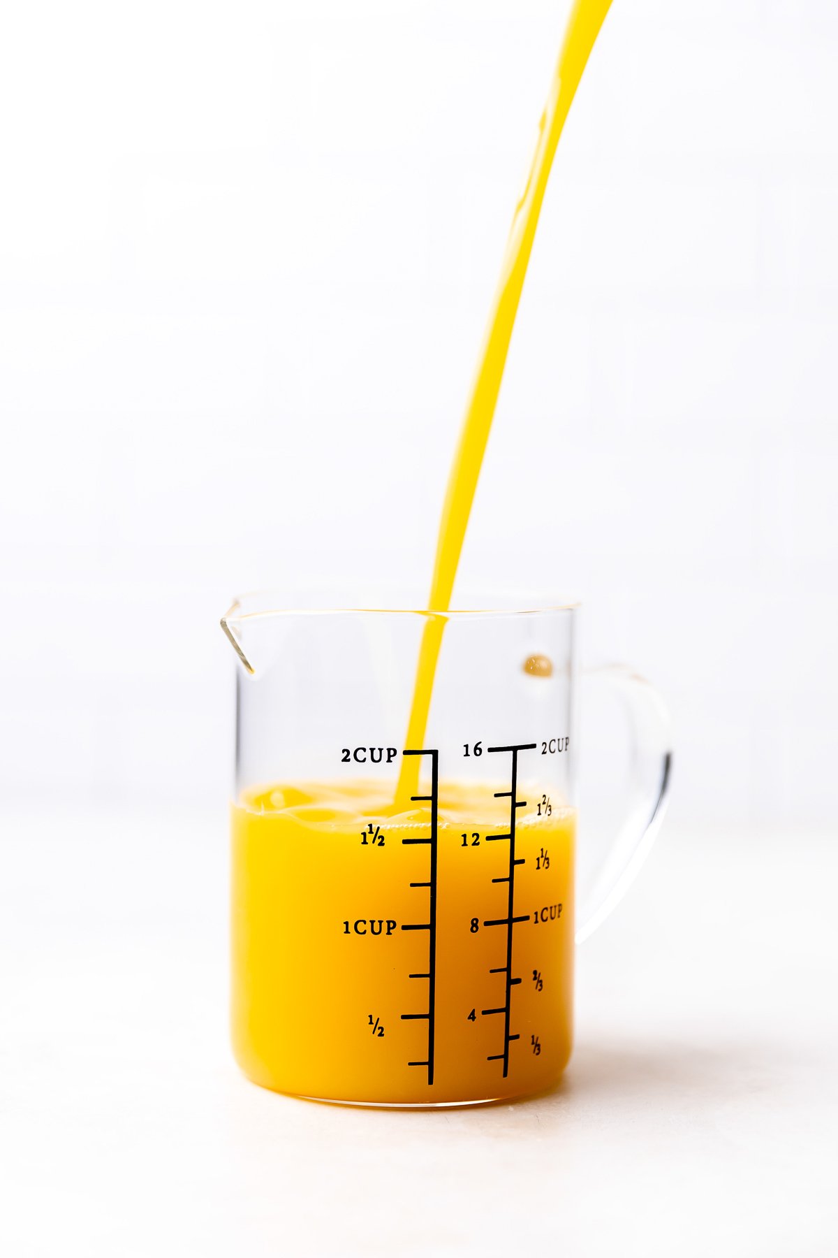 Florida orange juice is poured into a large glass measuring cup for orange chicken stir fry. The measuring cup rests atop a creamy white textured surface.