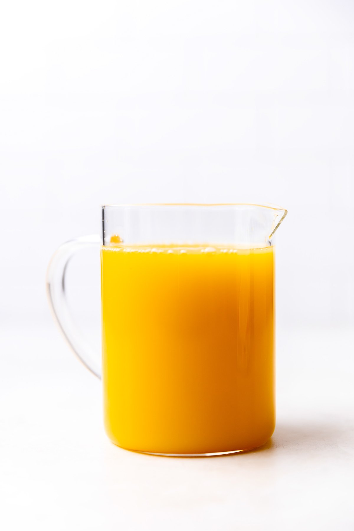 Florida orange juice fills a large glass measuring cup for orange chicken stir fry. The measuring cup rests atop a creamy white textured surface.