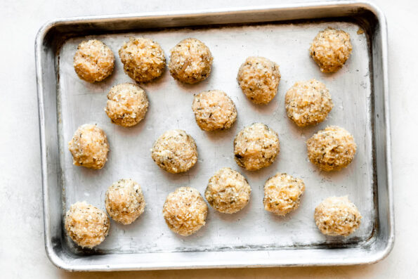 Eighteen formed chicken or turkey meatballs are arranged atop a metal baking sheet. The baking sheet sits atop a creamy white textured surface.
